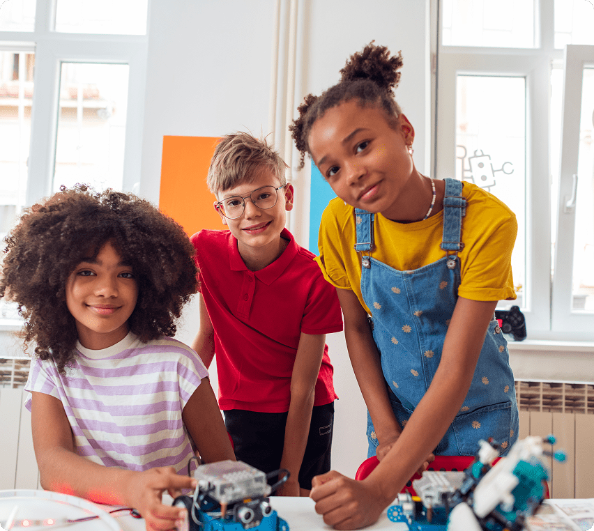 Three children happily working on a robotics project indoors.