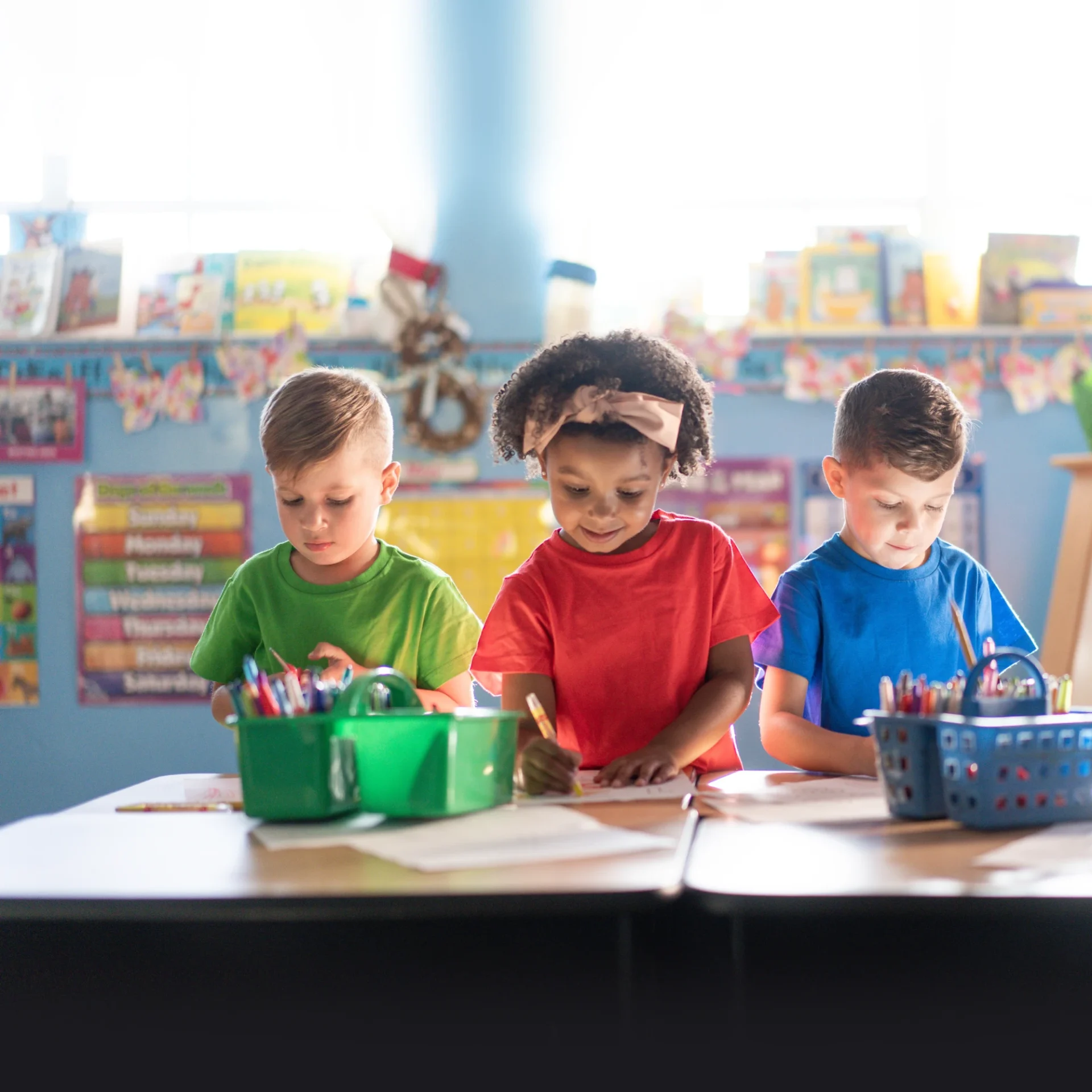 Three children engaged in crafting activities at a classroom table.