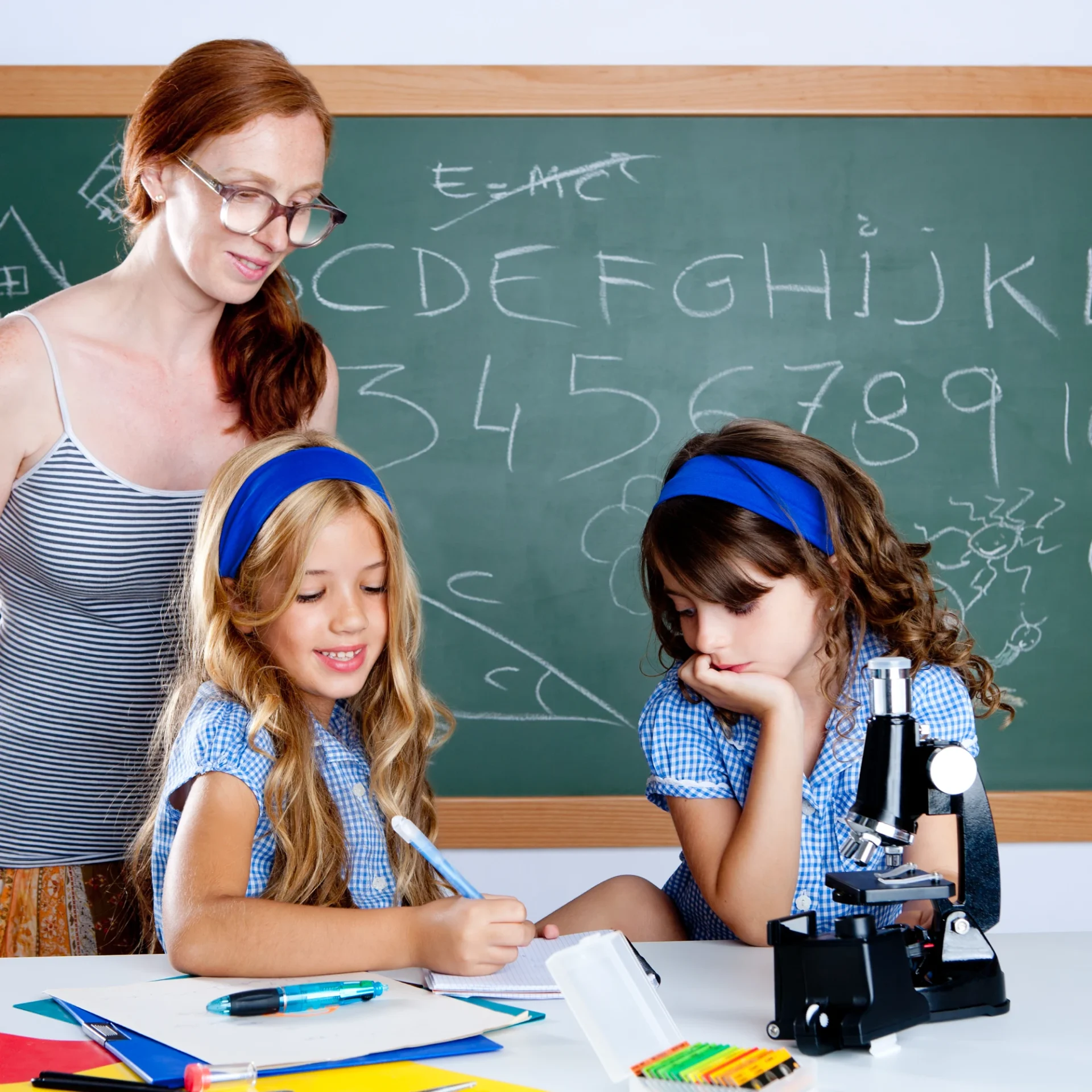 Teacher guiding two girls in a science class with a microscope.