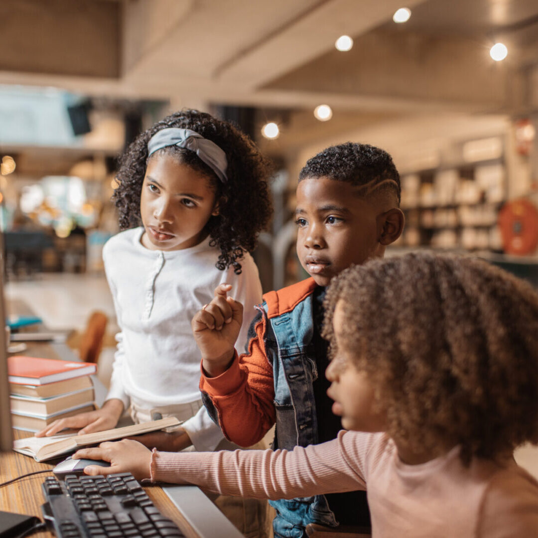 Three children exploring a computer in a cozy bookstore.