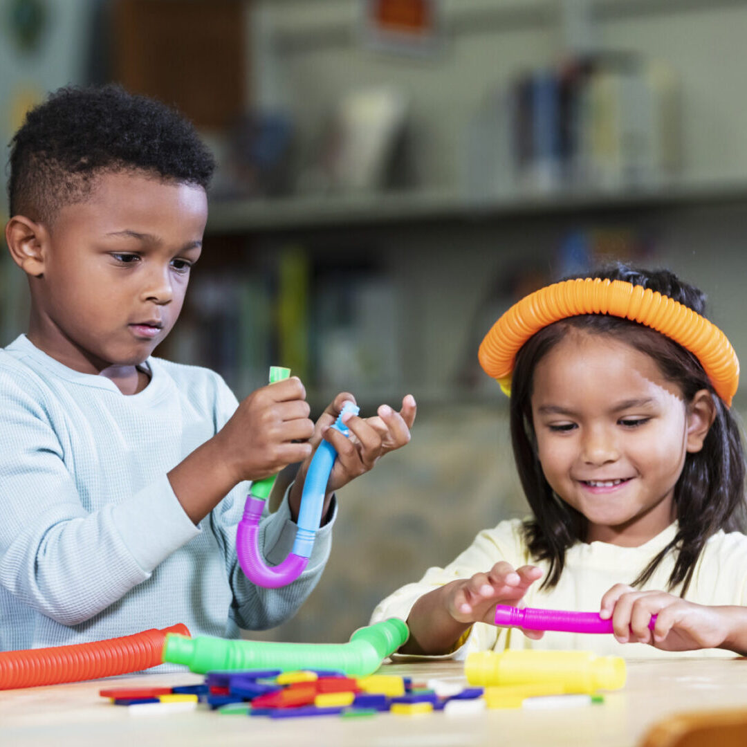 Two children engaged in arts and crafts at a table with colorful materials.